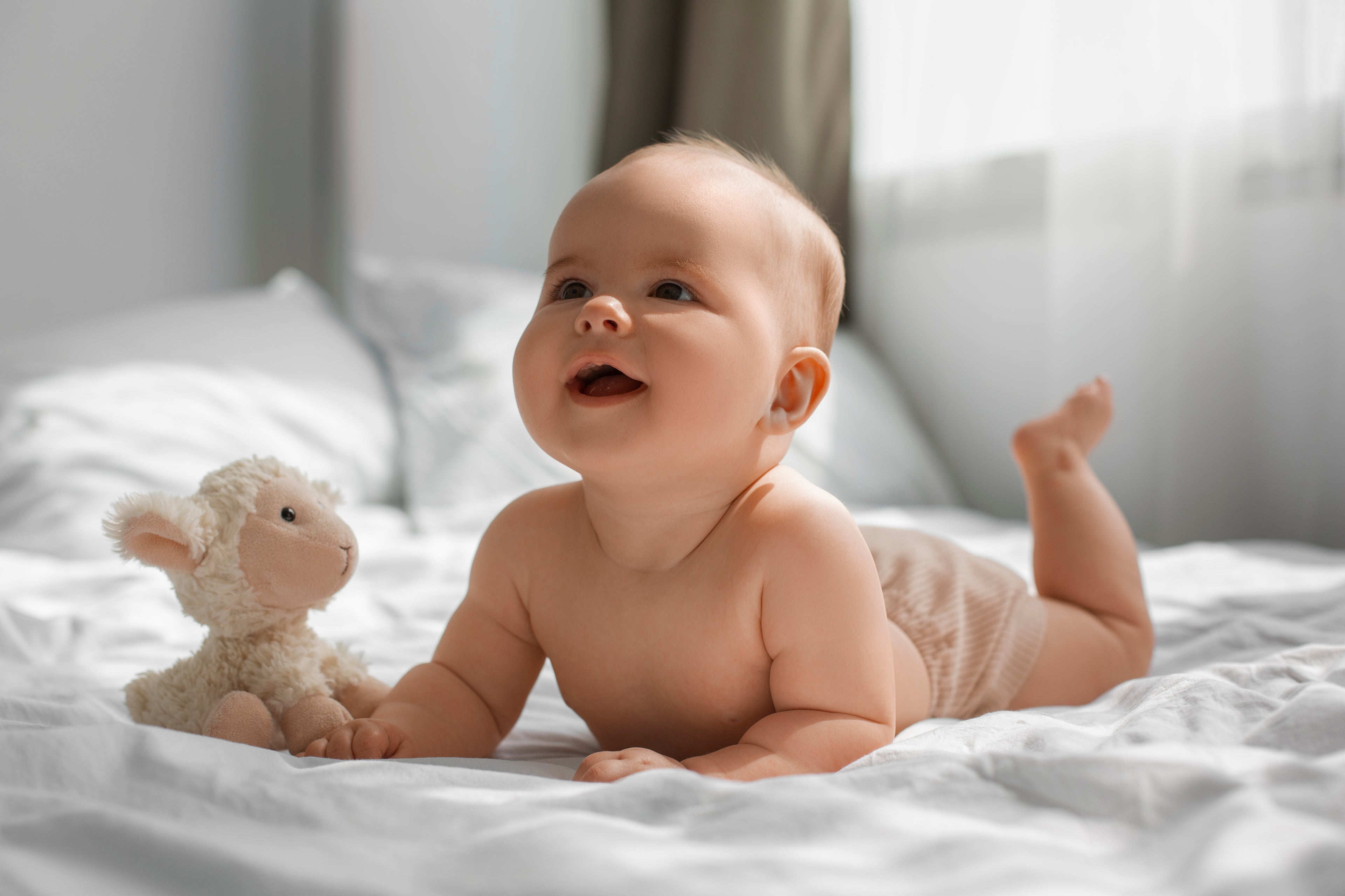 Baby lying on a bed with a plush toy