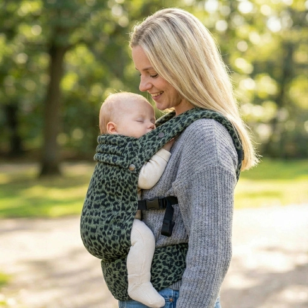 Woman carrying a baby in a green  leopard print carrier outdoors.