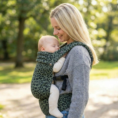 Woman carrying a baby in a green  leopard print carrier outdoors.